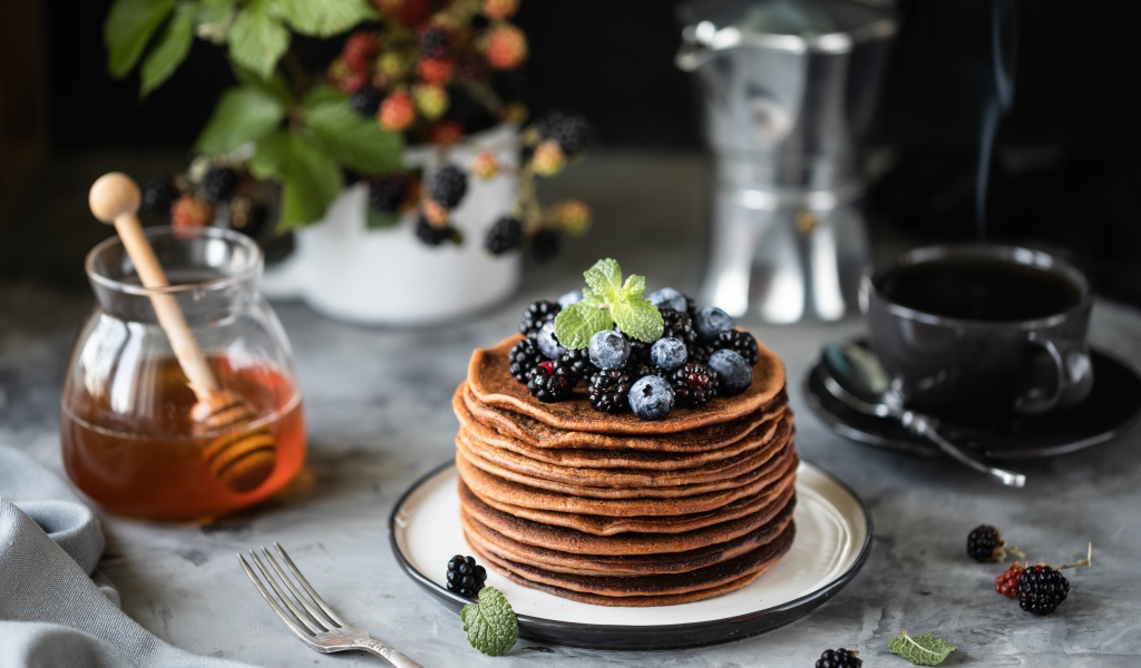 Гречневые блинчики с ягодами на столе с медом