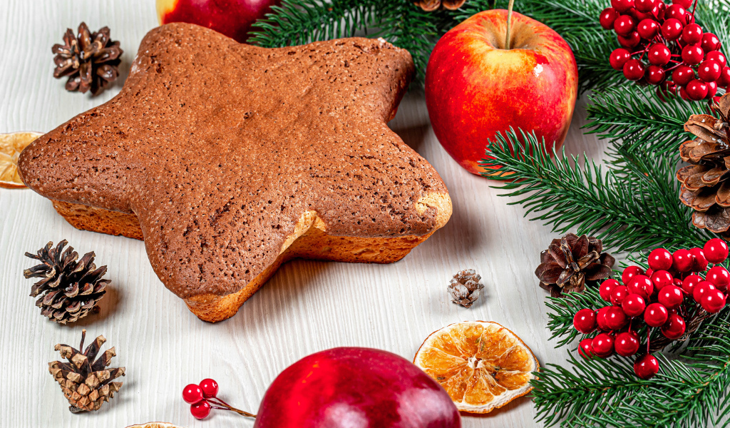 Рождественский кекс на столе с еловыми ветками,  яблоками и шишками