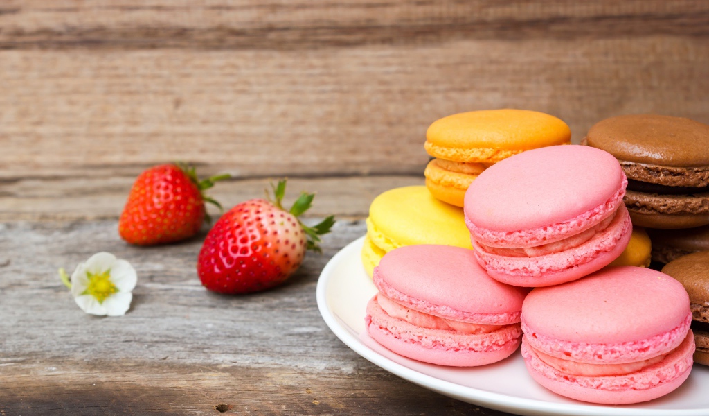 Разноцветный десерт макарун на белой тарелке на столе с клубникой