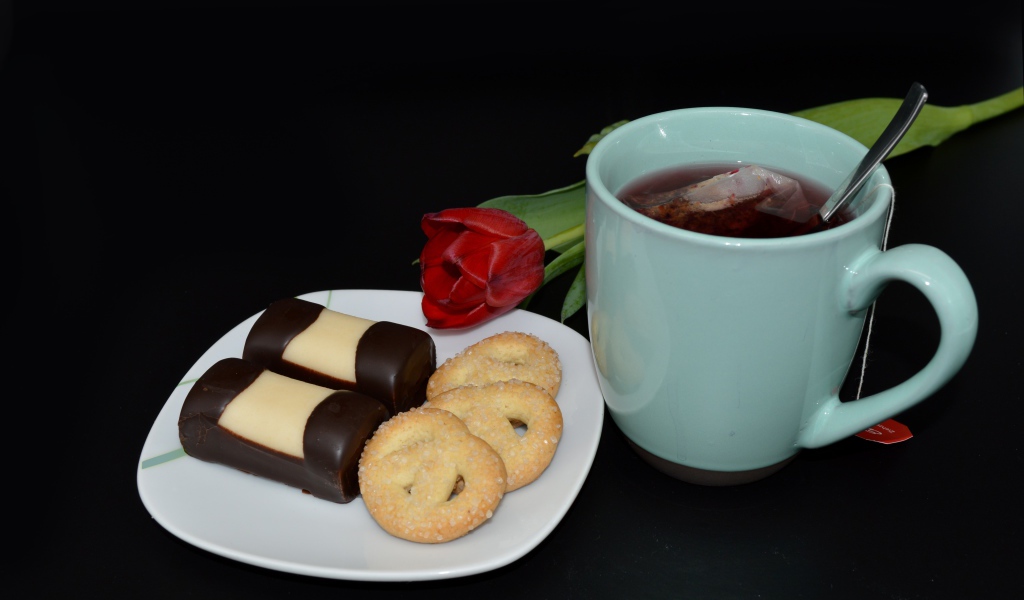 Печенье с конфетами на столе с чашкой чая и тюльпаном