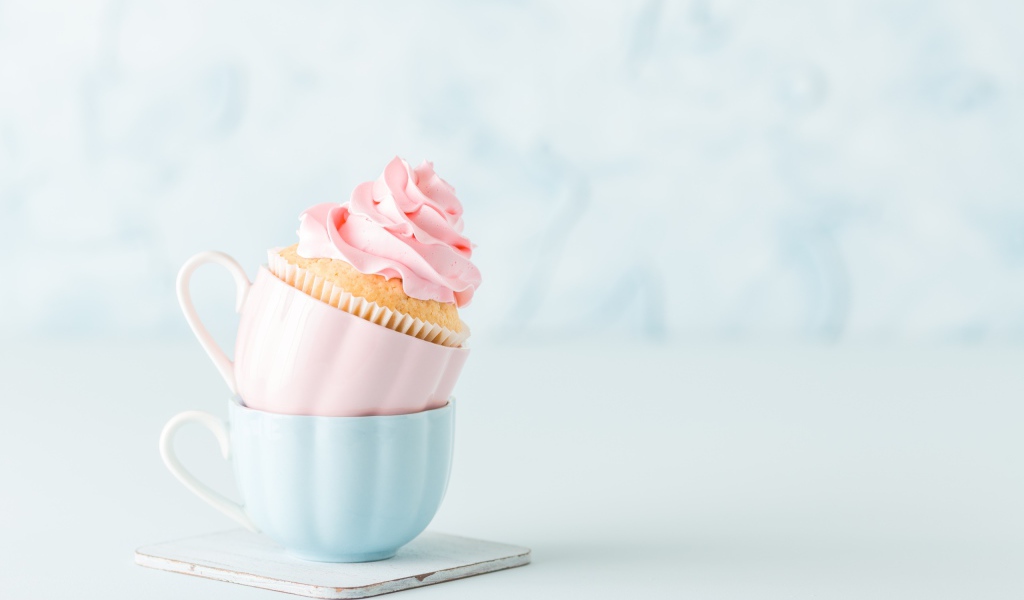 Кекс с розовым кремом с чашками на столе 