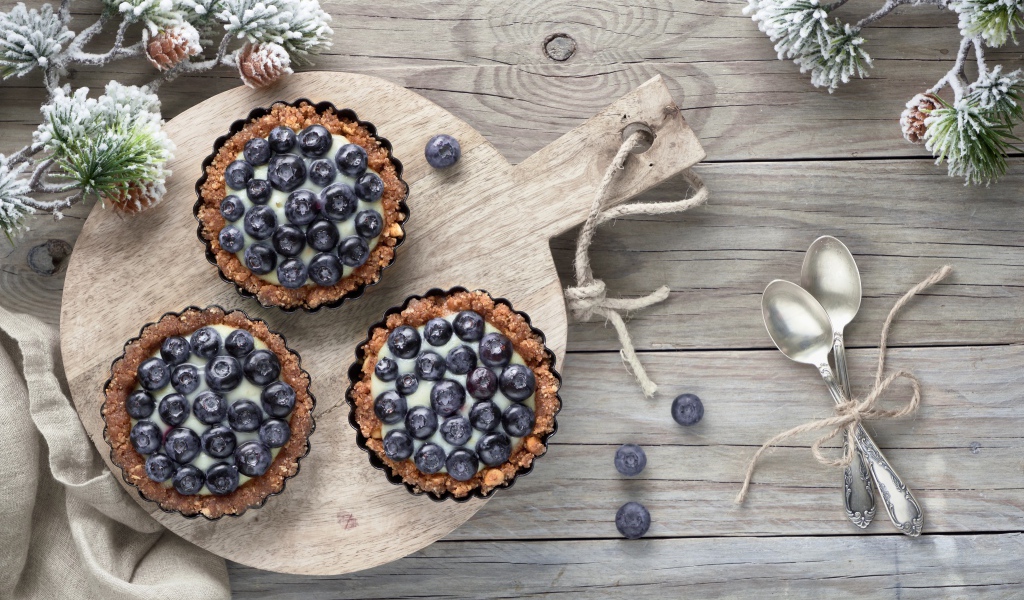 Кексы с кремом и ягодами черники на столе с чайными ложками