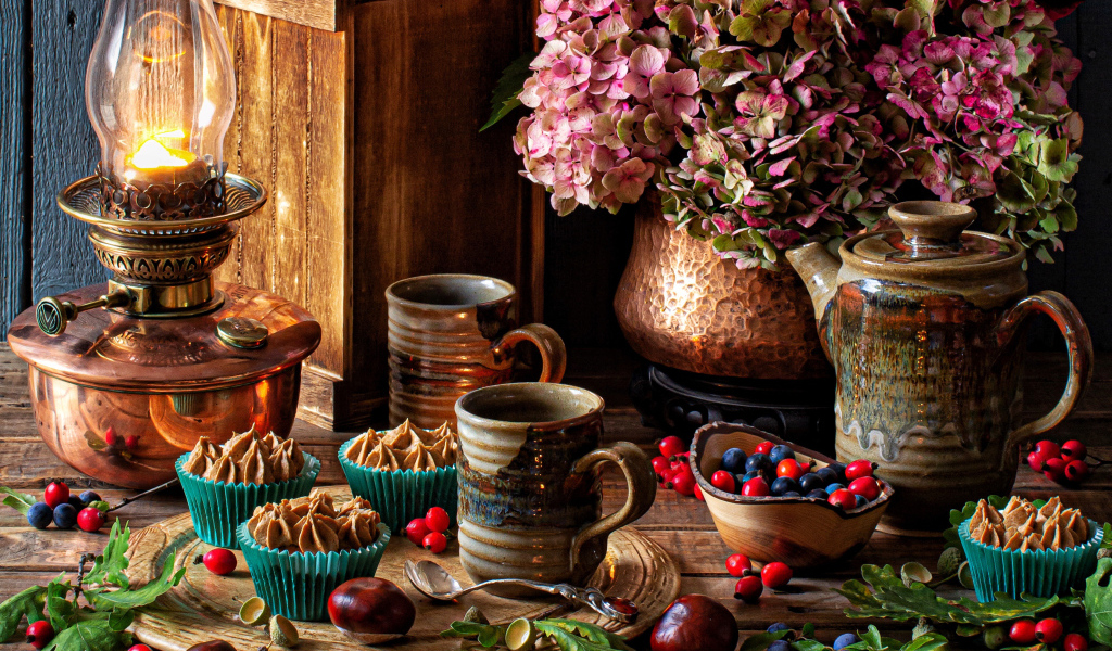 Кексы с кремом на столе с ягодами, цветами и лампой 