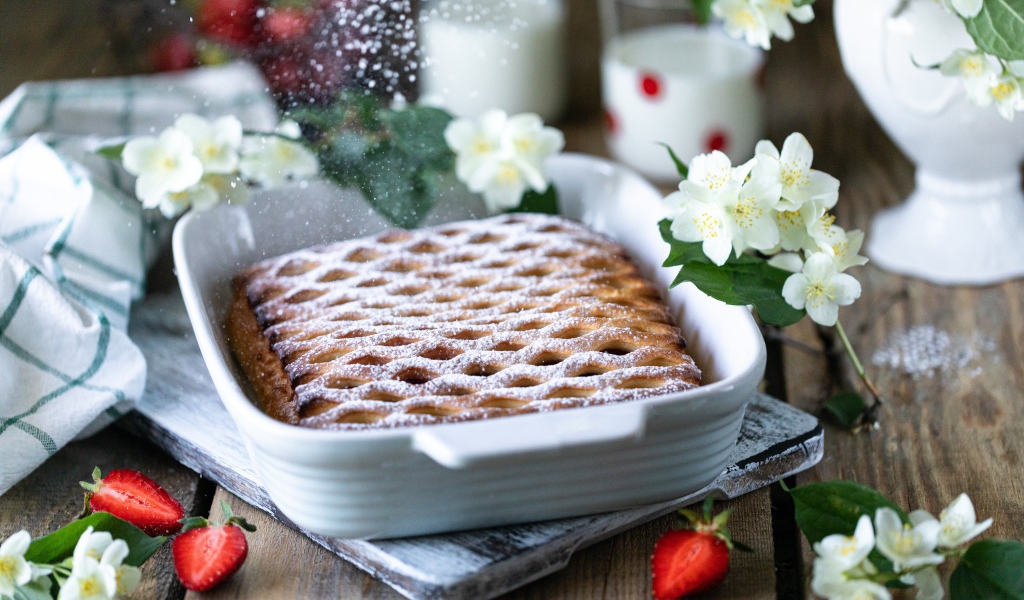 Вкусный клубничный пирог с сахарной пудрой на столе с цветами жасмина