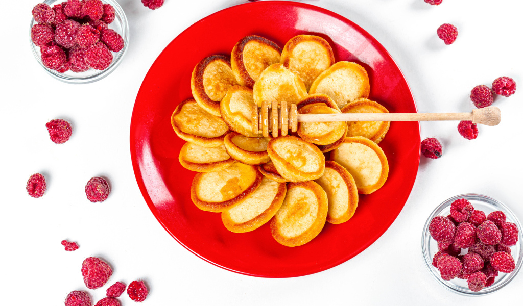 Оладьи на красной с медом на красной тарелке на столе с ягодами малины