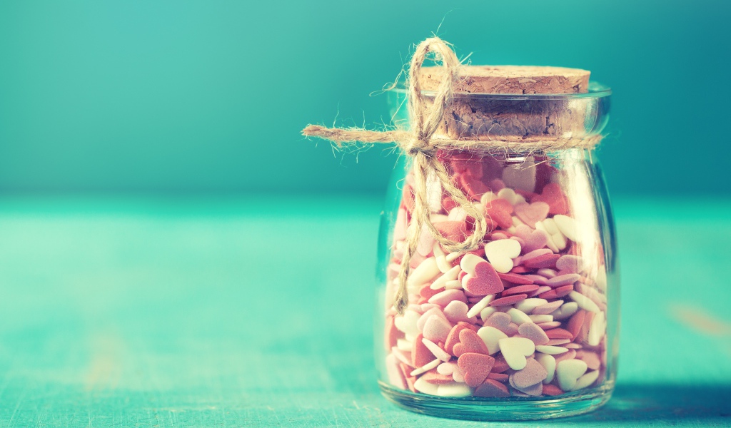 Стеклянная банка с маленькими конфетами в форме сердца на голубом фоне