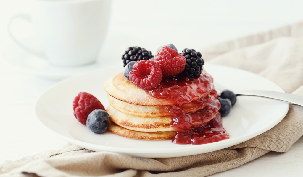 Оладьи на большой белой тарелке с джемом и ягодами 