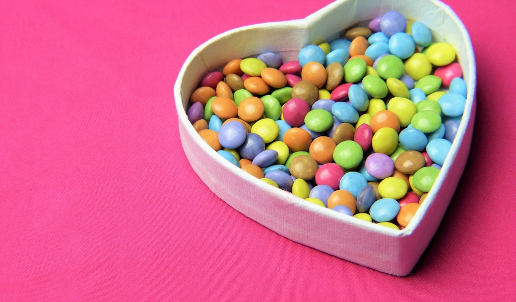 Коробка в форме сердца с разноцветными конфетами на розовом фоне