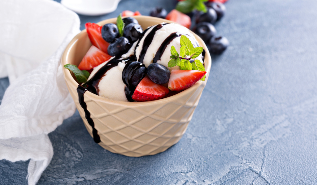 Шарики мороженого в стакане на столе с клубникой и ягодами черники