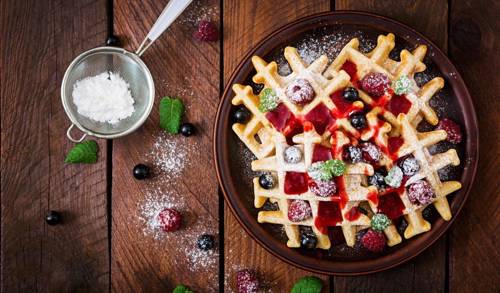 Сладкие медовые вафли на тарелке с ягодами и джемом и сахарной пудрой 