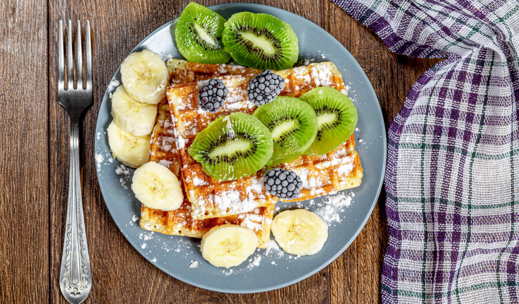 Сладкие вафли на тарелке с сахарной пудрой, бананами и киви