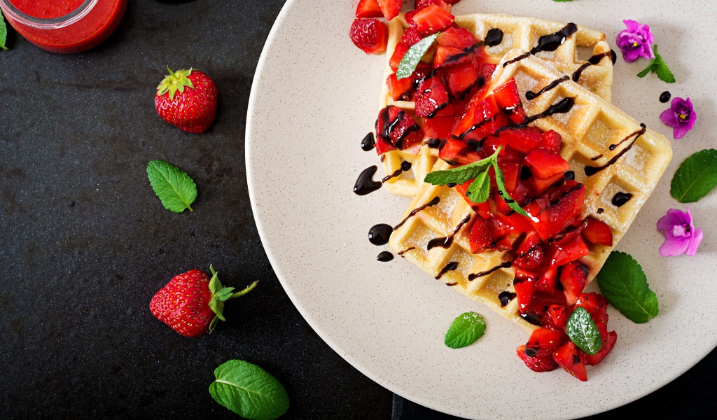 Сладкие вафли на тарелке с кусочками клубники