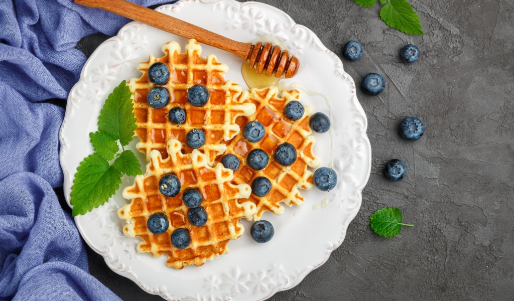 Сладкие вафли с медом на тарелке с ягодами черники