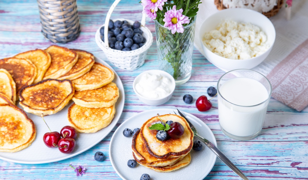 Вкусные оладьи на столе с ягодами черники, творогом и молоком