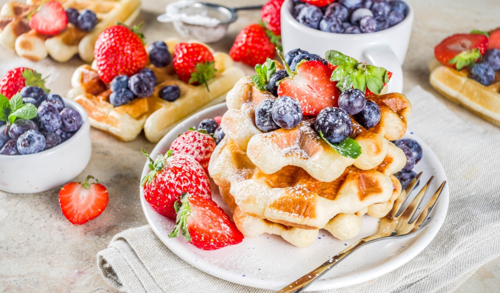 Вкусные сладкие вафли с ягодами клубники, черники и сахарной пудрой