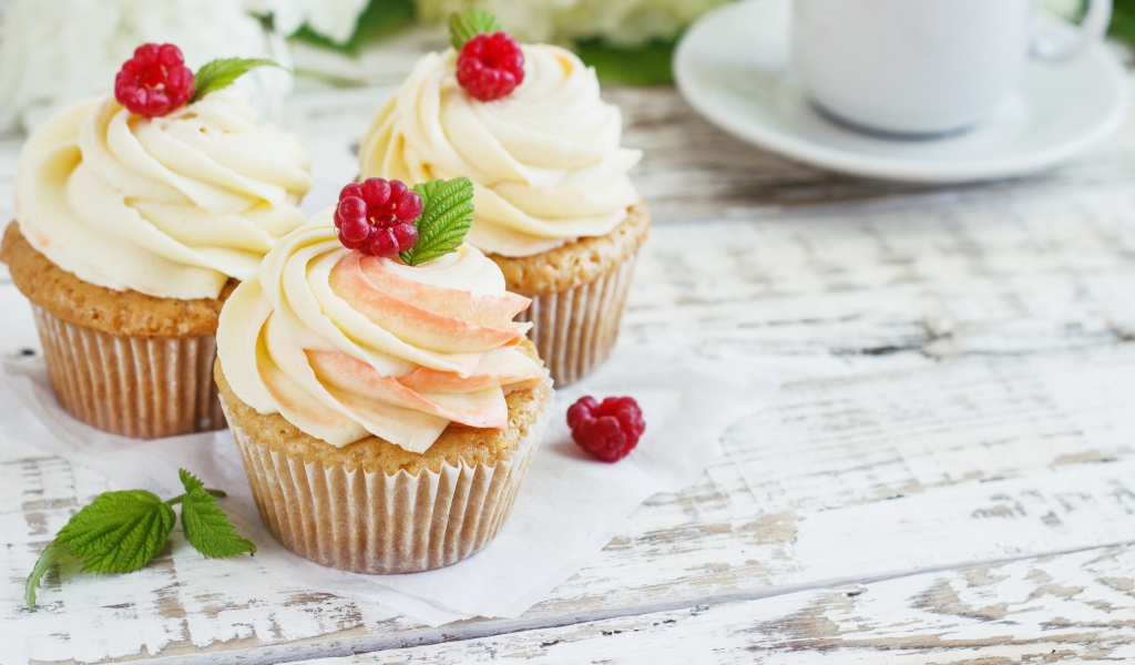 Три кекса с кремом на столе с чашкой кофе