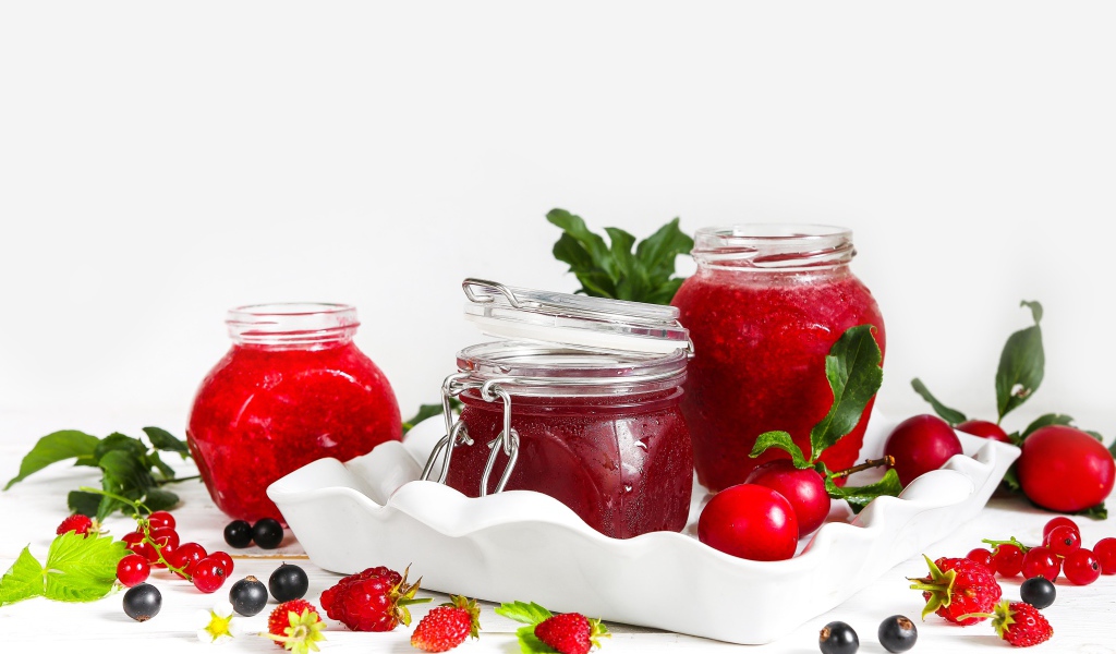 Три банки джема с ягодами на белом фоне