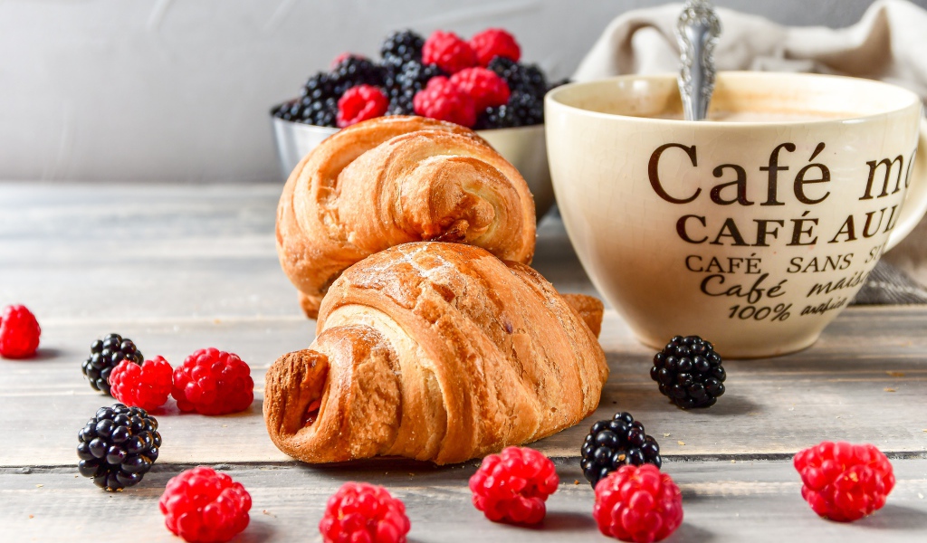Два круассана с малиной, черникой и чашкой кофе на столе