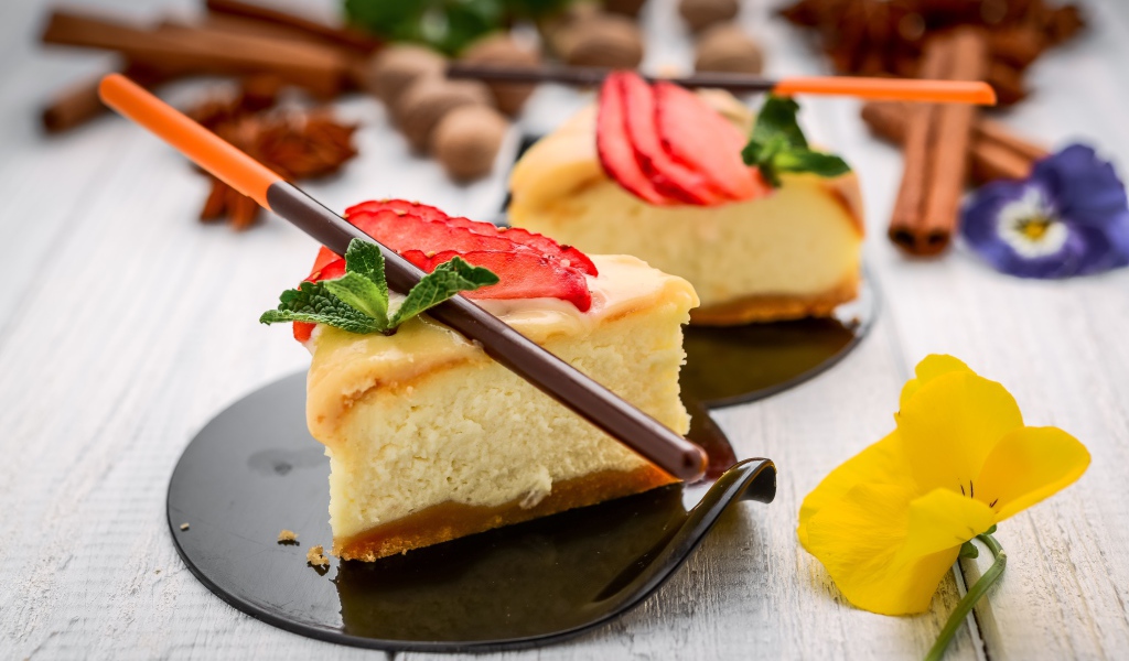 Два куска чизкейка с клубникой на столе с палочками