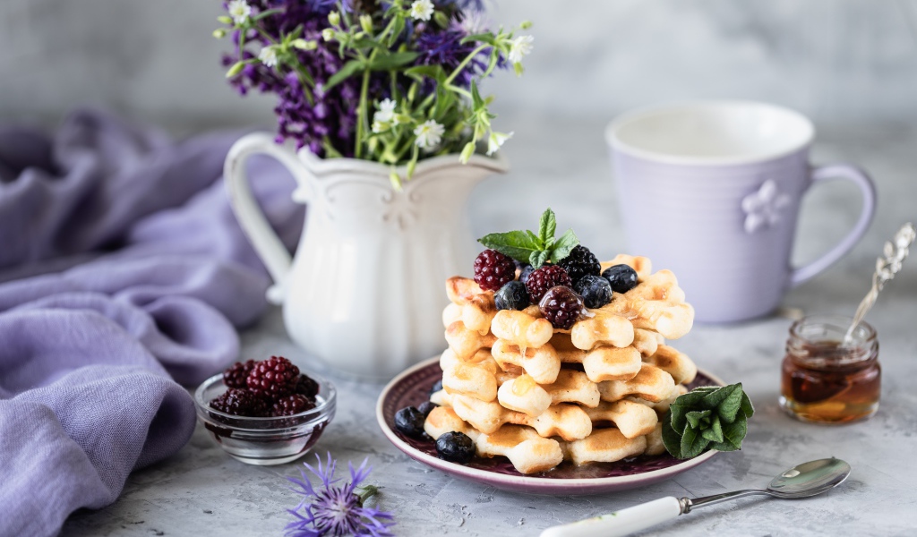 Вафли с ягодами черники и ежевики на столе с букетом