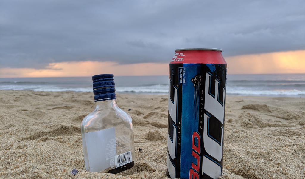 Бутылка пива и бутылка водки на песке у моря