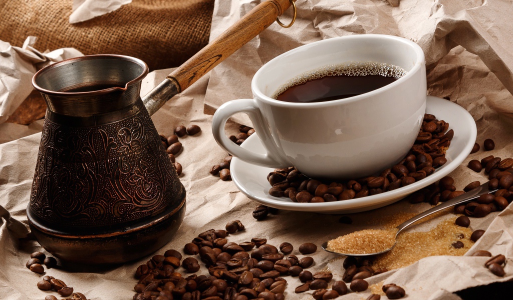 Чашка горячего кофе на столе с туркой, зернами и коричневым сахаром