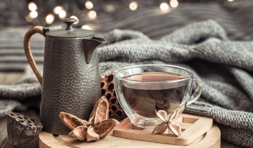 Чашка чая на столе с чайником и теплым пледом