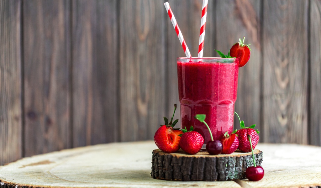 Стакан ягодного смузи на столе с клубникой и вишней