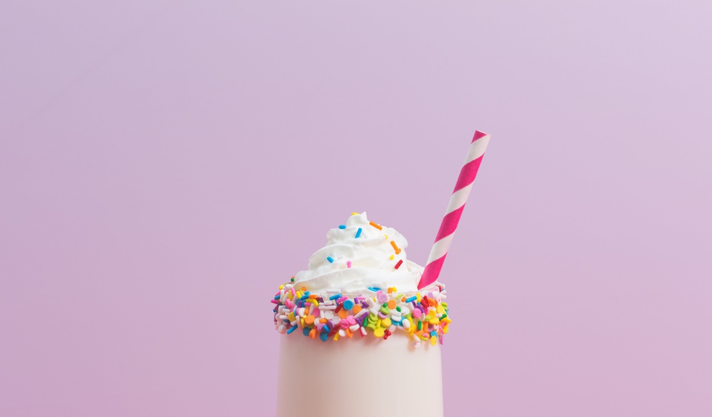 Коктейль  в стакане со взбитыми сливками на розовом фоне