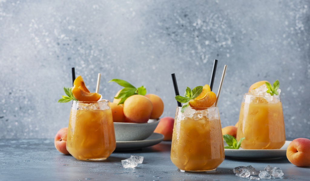Холодный абрикосовый напиток со льдом в стаканах на столе со свежими абрикосами