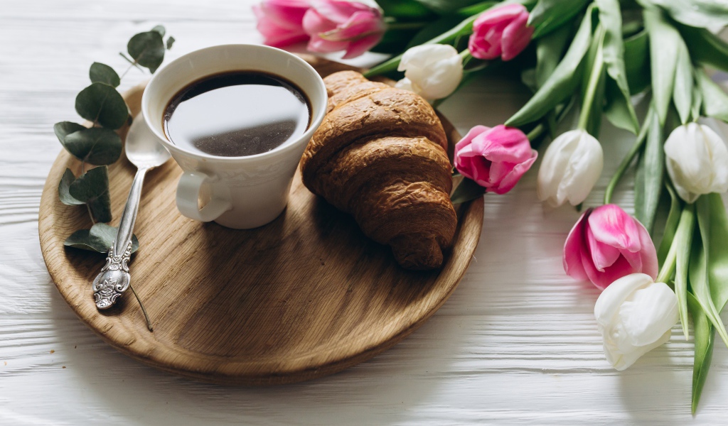 Чашка кофе и круассан на столе с букетом тюльпанов