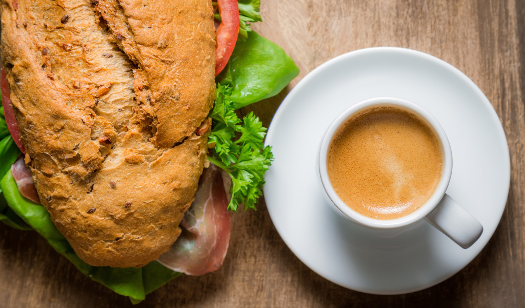 Чашка кофе с бутербродом на столе к завтраку 