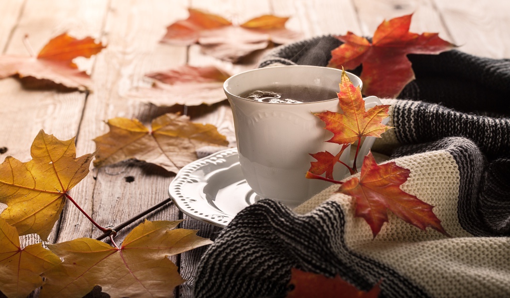 Чашка чая на столе с осенними листьями и пледом