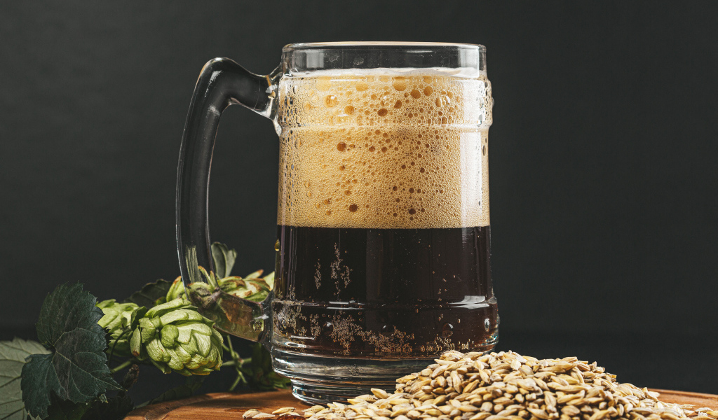 Темное пиво в бокале на столе с хмелем и зернами пшеницы 