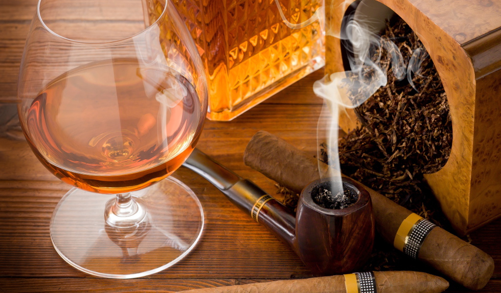 Бокал коньяка на столе с трубкой и сигарой 