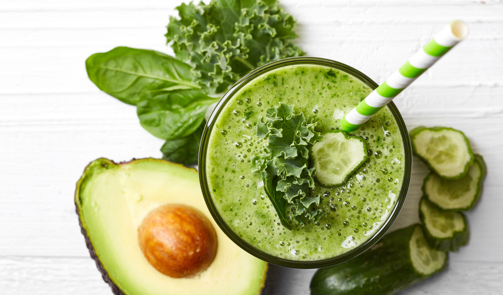 Зеленый смузи на столе с огурцом, авокадо и зеленью