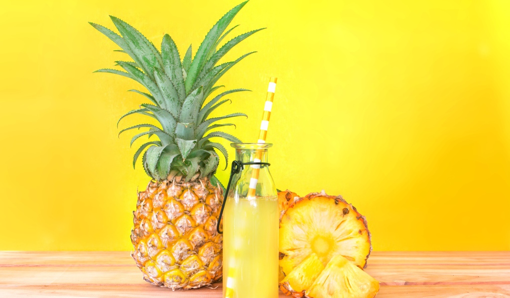 Сок в бутылке на столе с ананасами