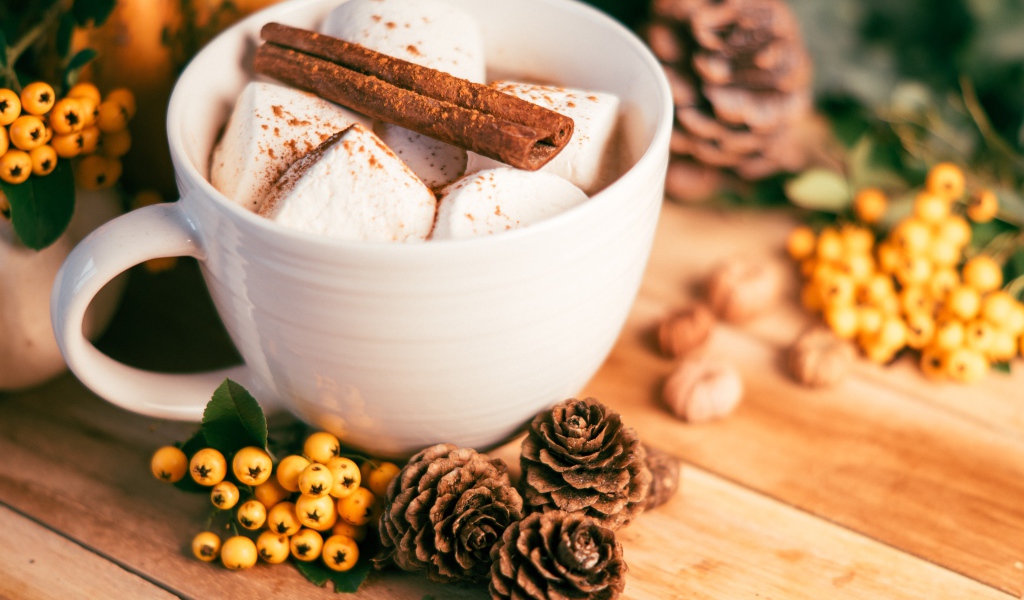 Маршмеллоу в чашке с корицей на столе с шишками и гроздьями рябины