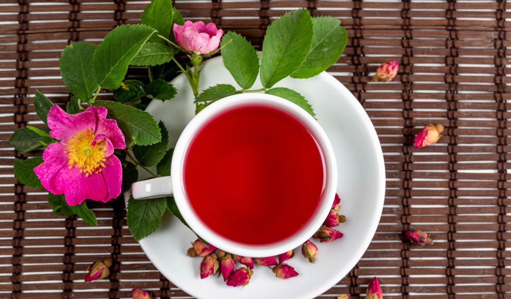 Красный чай с шиповника на столе с цветами
