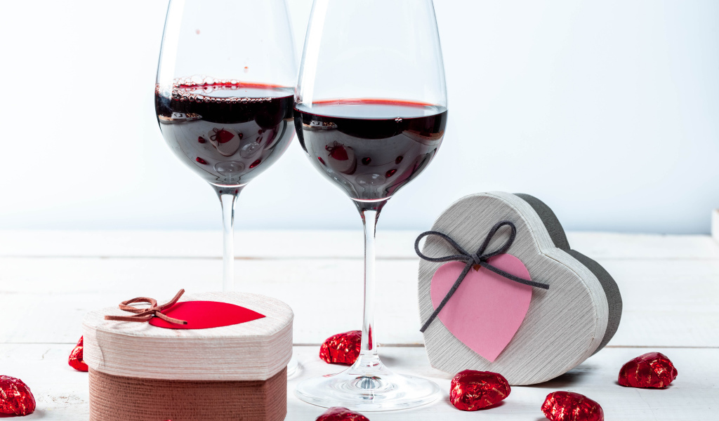 Две коробки с конфетами в форме сердца на столе с бокалами 