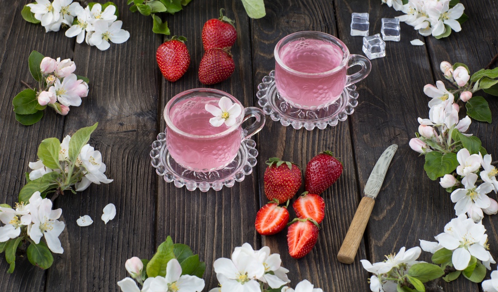 Две стеклянные чашки ягодного чая на столе с клубникой и цветами яблони