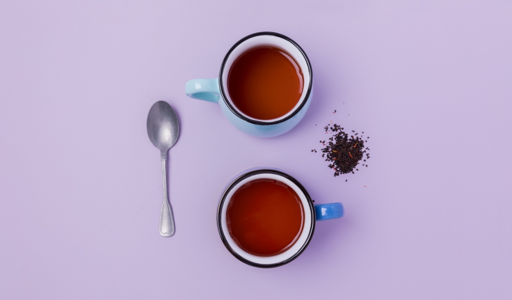 Две железные чашки чая на сиреневом фоне с ложкой