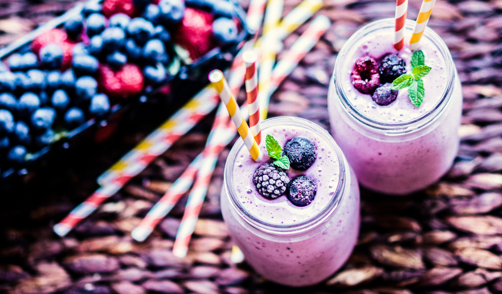 Две банки смузи с трубочками на столе с ягодами