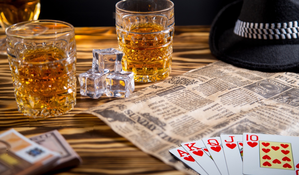 Виски со льдом на столе с картами, газетой и шляпой