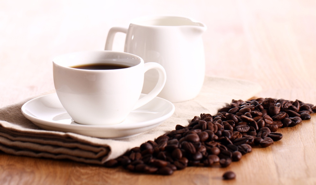 Белая чашка кофе на столе с молоком и зернами