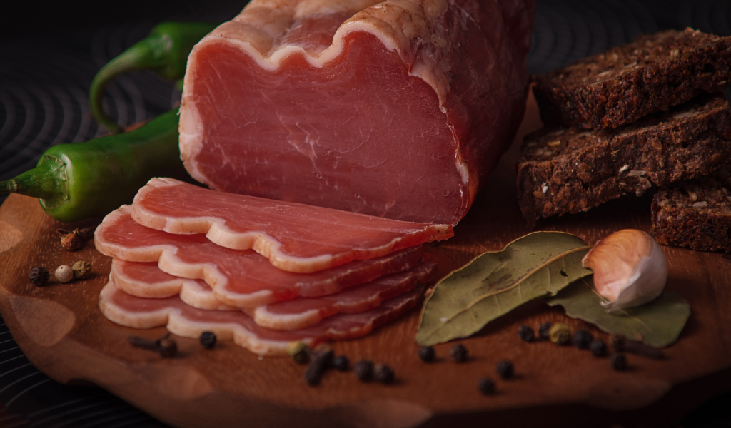 Кусок вяленого мяса на доске с черным хлебом и специями