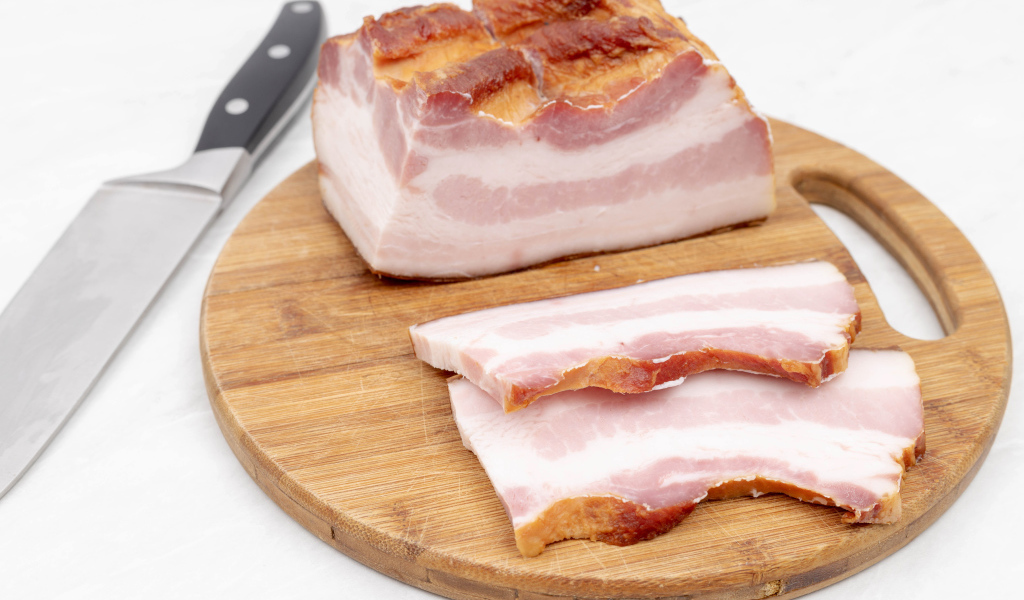 Кусок вкусного копченого сала на доске с ножом