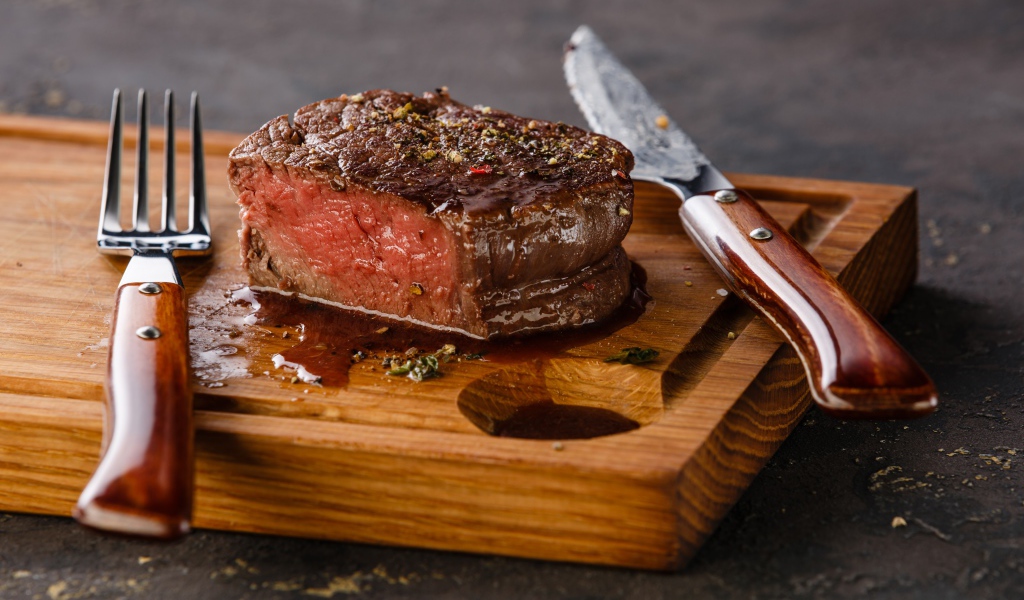 Кусок сочного мяса на доске с ножом и вилкой 