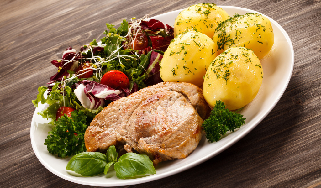 Кусок мяса на тарелке с картофелем и салатом