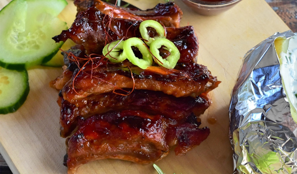 Аппетитные жареные ребрышки на столе с огурцами  и соусом 